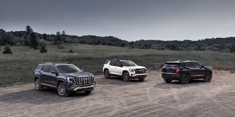 Three GMC SUVs parked on a gravel trail in a scenic outdoor landscape
